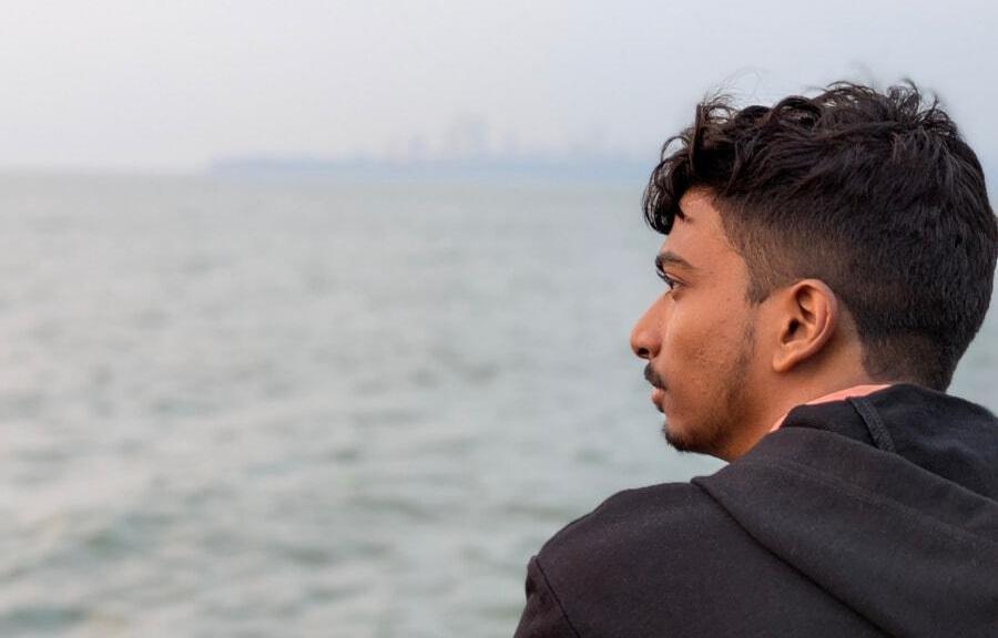 A picture of Pranav Chakkarwar looking to his left. Sea water and city's skyline are visible in the background but are blurred because the picture was captured in portrait mode.